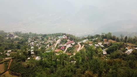 Una-Toma-Aérea-De-Una-Ciudad-Rural-En-La-Cima-De-Un-Valle-Neblinoso-En-Las-Colinas