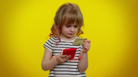 Little-teen-kid-child-girl-using-credit-bank-card-and-smartphone-while-purchases-online-shopping