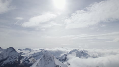 Aerial-tilt-down-shot-snowy-mountain-peaks-lighting-by-sunlight-and-blue-colored-lake-in-the-valley---Zell-Am-see,-Kitzsteinhorn-Mountain-in-Austria