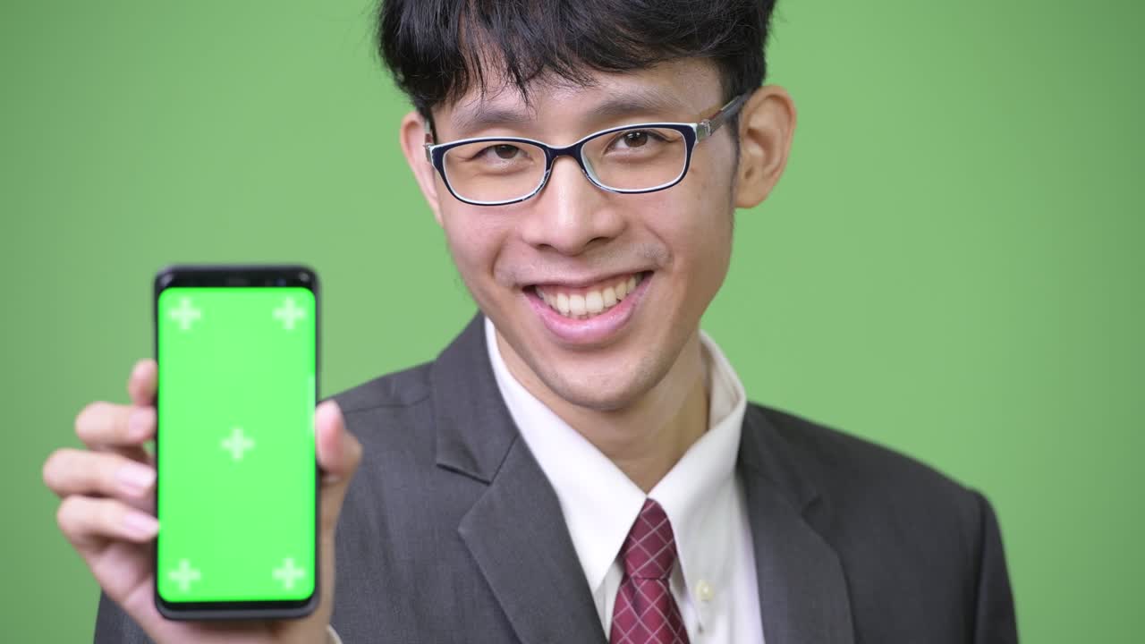 젊은 행복한 아시아 사업가 가 카메라 에 전화 를 보여주면서 미소 짓고 있다