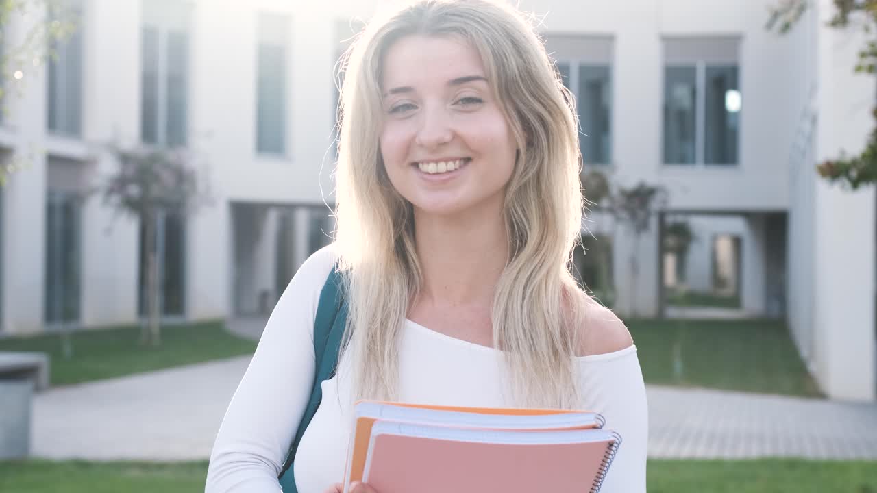 Giovane donna bionda e allegra che tiene in mano un libro nel campus universitario