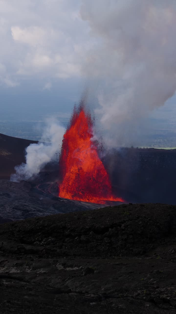 Ripresa verticale in slow motion 4K di una fontana di lava che erutta all'interno del cratere Kīlauea, che mostra schizzi di lava incandescente e una densa colonna di fumo vulcanico