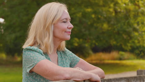 portrait of casually dressed mature or senior woman leaning on fence on walk in countryside