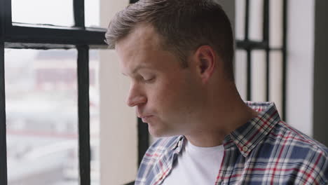 portrait-attractive-caucasian-man-using-smartphone-drinking-coffee-at-home-enjoying-relaxed-morning-browsing-messages-looking-out-window-texting-social-media-sharing-lifestyle-online-close-up