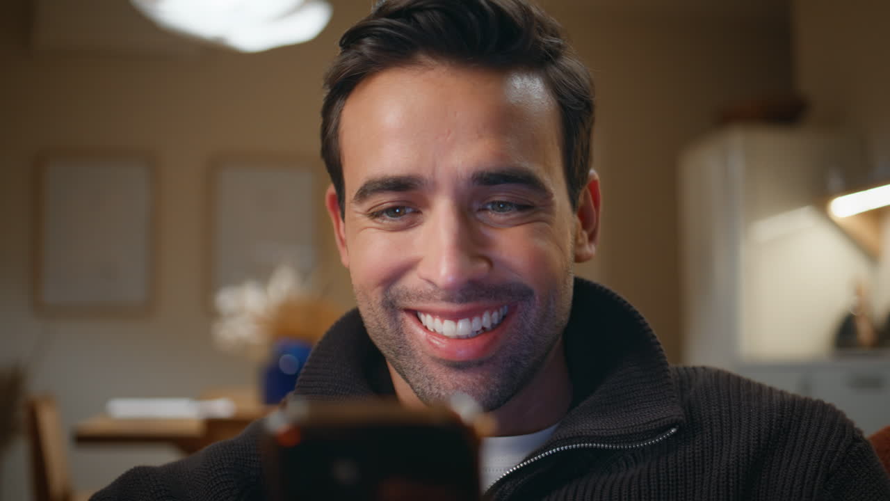Cheerful man watching smartphone video content in evening living room closeup