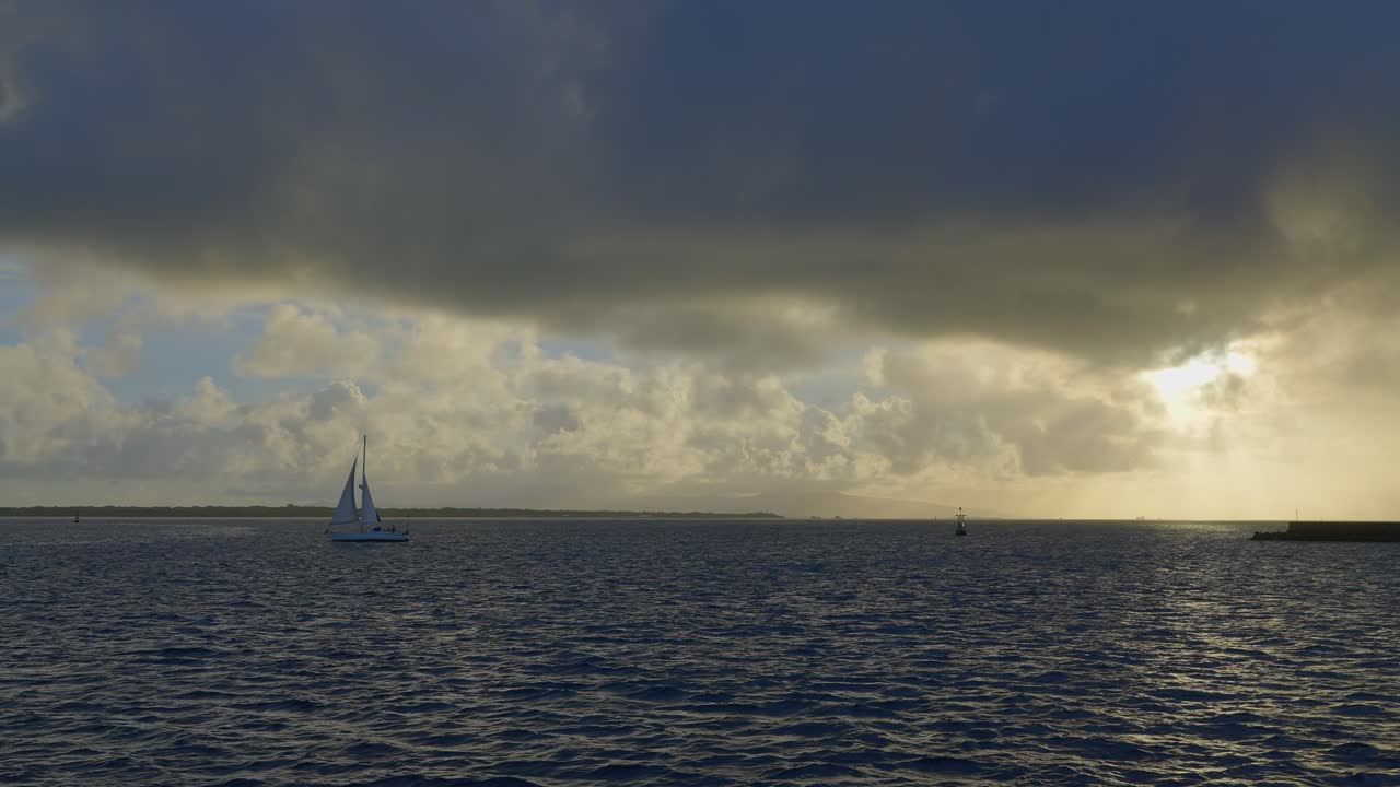 From a boat's perspective, a mesmerizing shot of vast sunset clouds, bathed in divine rays, with a sailboat leisurely navigating nearby