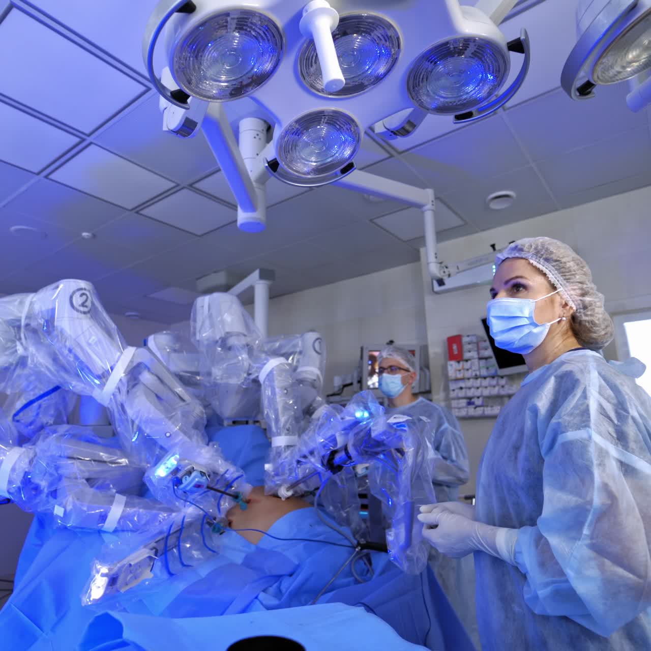 Surgery with robotic equipment in hospital. Minimally invasive surgery in modern operating room. Female doctor observes the work of robotic machine.