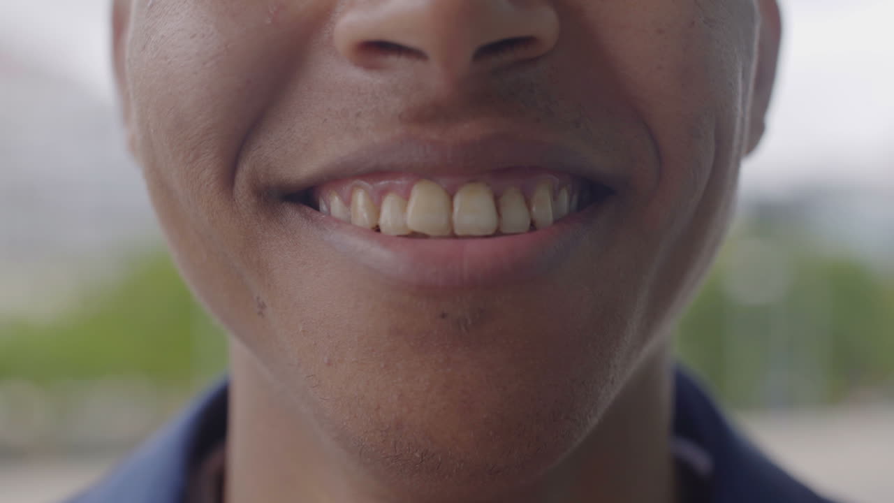 un primer plano de un joven afroamericano sonriendo al aire libre.