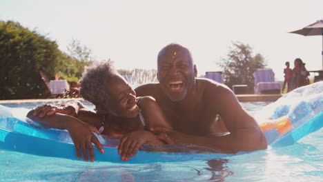 portrait of smiling senior couple on summer holiday relaxing in swimming pool on inflatable airbed