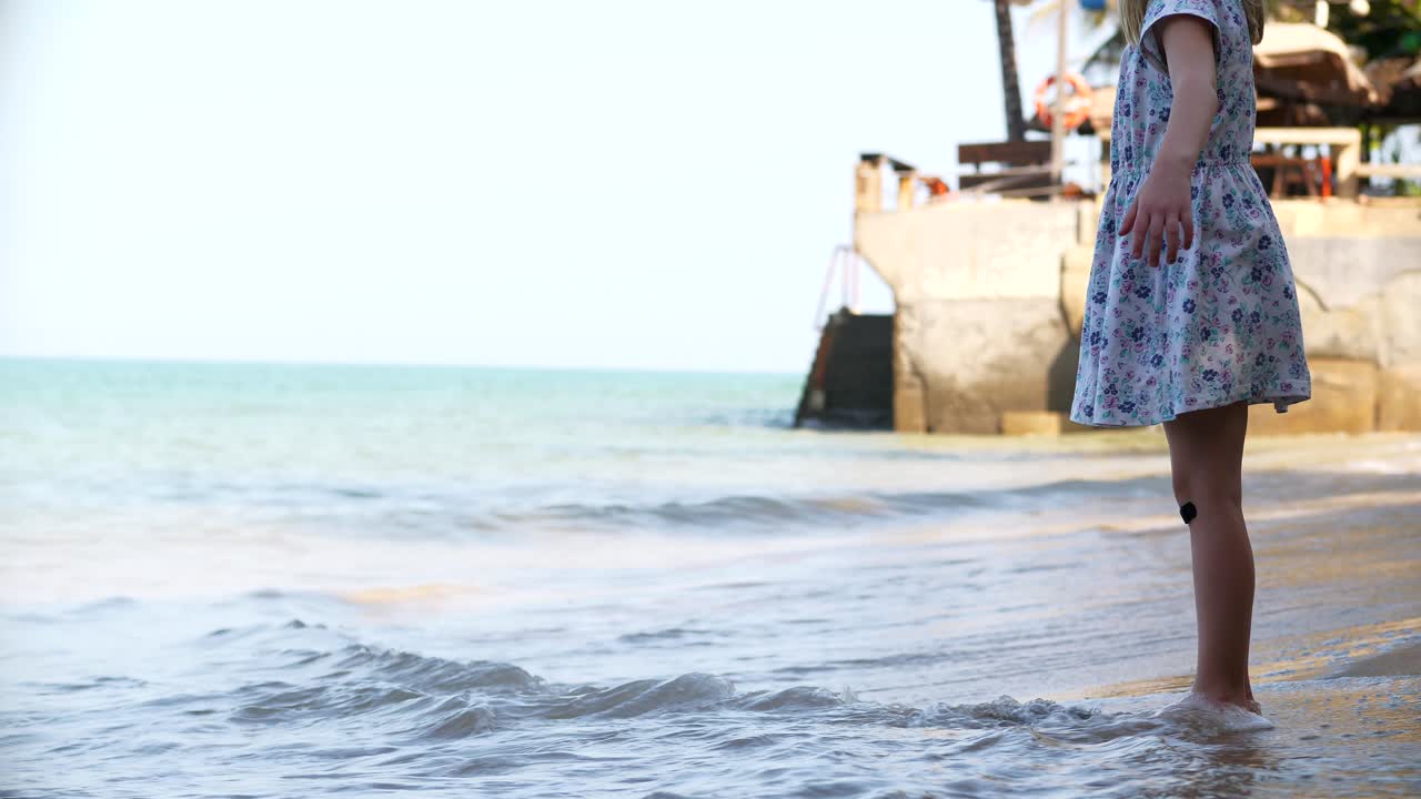 어린 소녀는 해변 해안 파도에서 물러납니다.