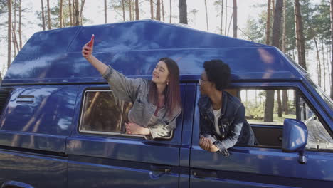 dos hermosas chicas se toman un selfie asomándose por la ventana de una caravana durante un viaje por carretera 1