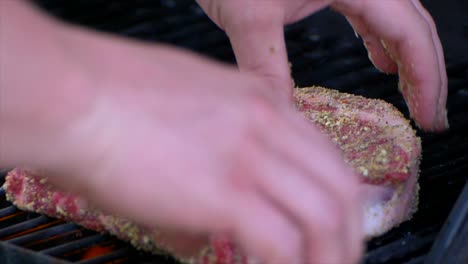 dos manos ponen un filete grueso de costilla cruda en una parrilla comenzando su proceso de asado