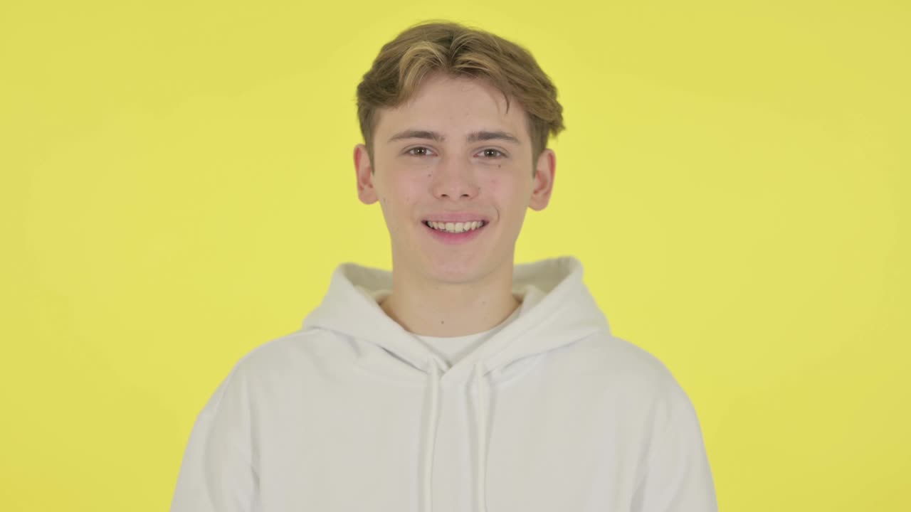 노란색 배경 에 있는 카메라 에 미소 짓는 젊은 남자