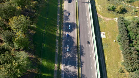 aerial - top down over the expressway - cars moving in two directions - road located close to trees, forest, and green belt - modern road construction in the center of agglomeration