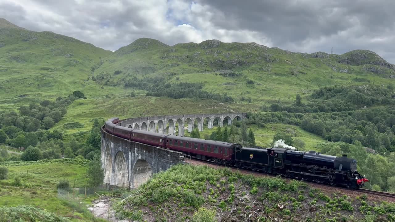 Establishing shot of a vintage steam train crossing Scotland’s iconic Glenfinnan Viaduct, white steam billowing against vibrant green mountains, evoking the legacy of the Industrial Revolution