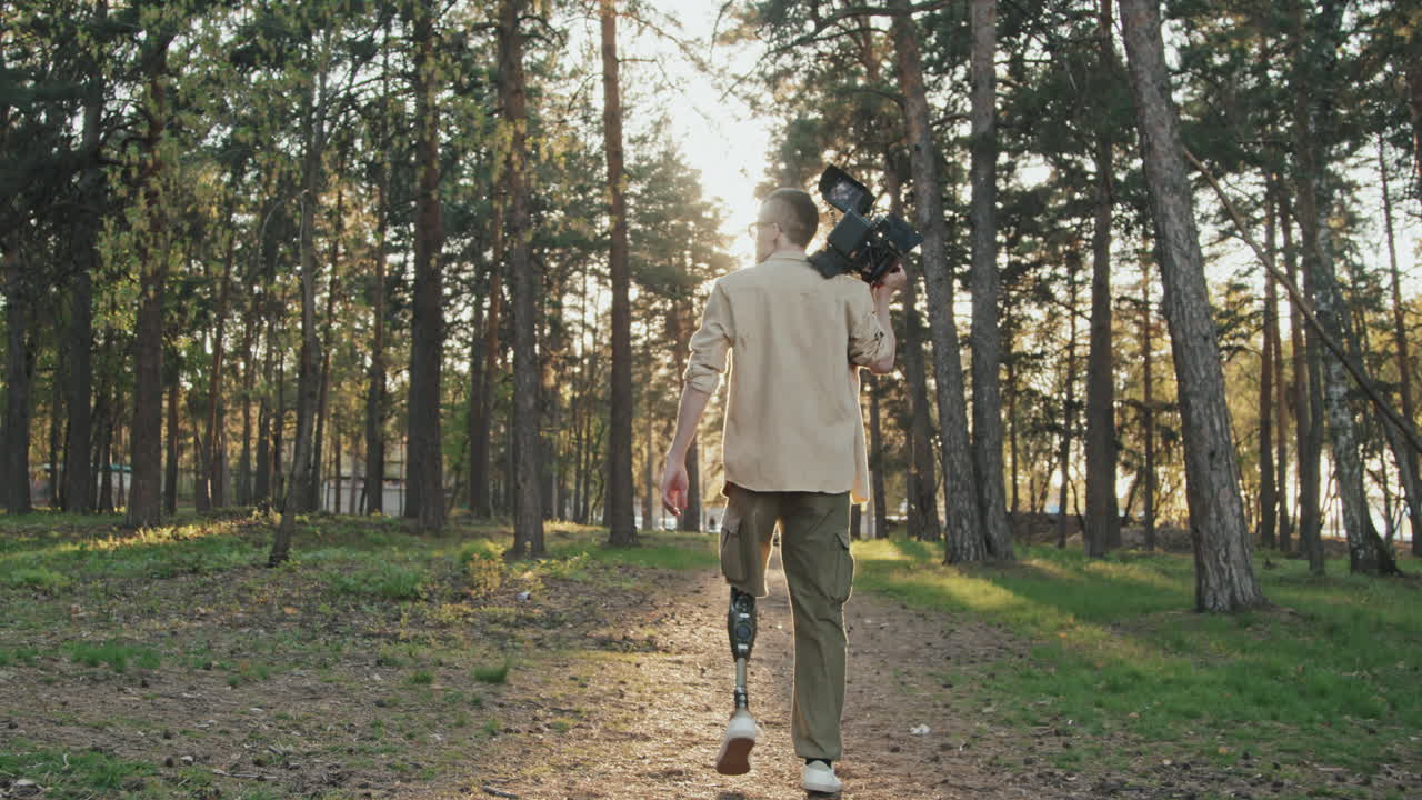 Rear-View Of Cameraman With Leg Prosthesis Walking In Forest