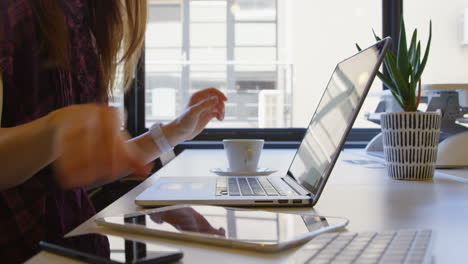 Mid-section-of-young-businesswoman-drinking-coffee-while-using-mobile-phone-at-desk-in-office-4k