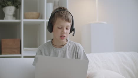 internet addicted little boy is using laptop for communicating and games sitting on bed and drawing on paper