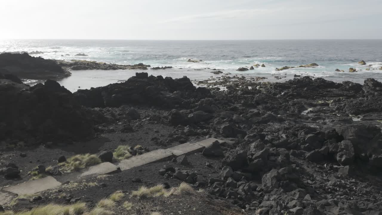 Rocky shore of Mosteiros, Sao Miguel with tumultuous sea and cloudy skies, showcasing rugged black volcanic terrain
