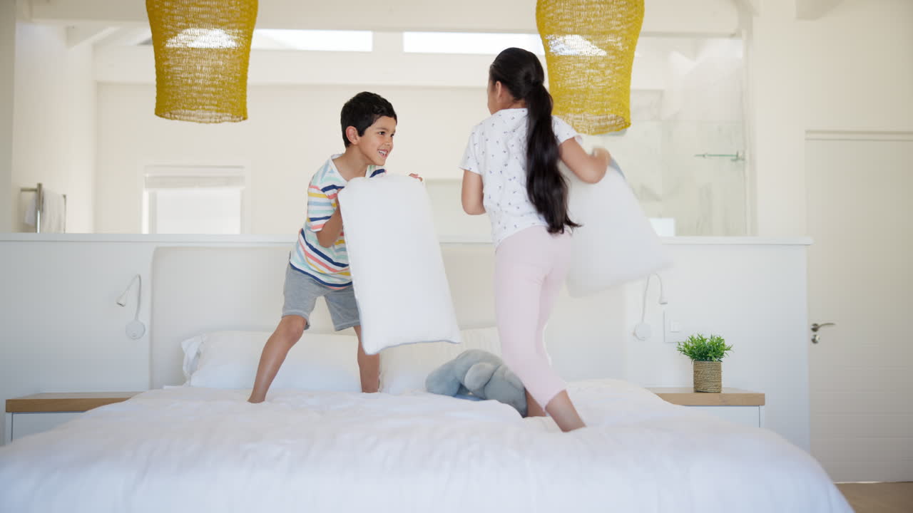 행복한 형제자매들이 침실에서 베개 싸움을 하고 있습니다.