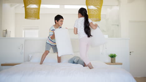 hermanos felices teniendo una pelea de almohadas en el dormitorio