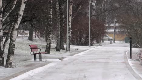 banco vazio sentado ao lado de um caminho gelado em um parque sem ninguém à vista durante uma tempestade de neve