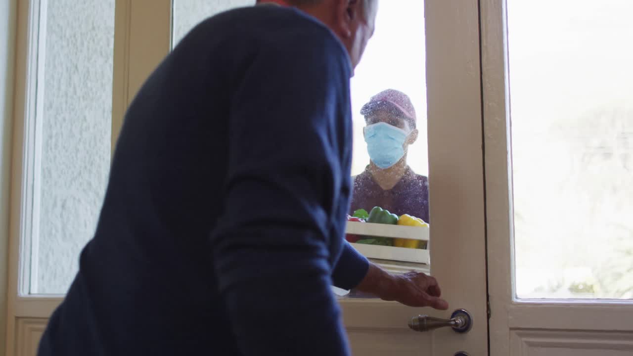 hombre de entrega con máscara facial entregando comestibles a un hombre mayor en casa