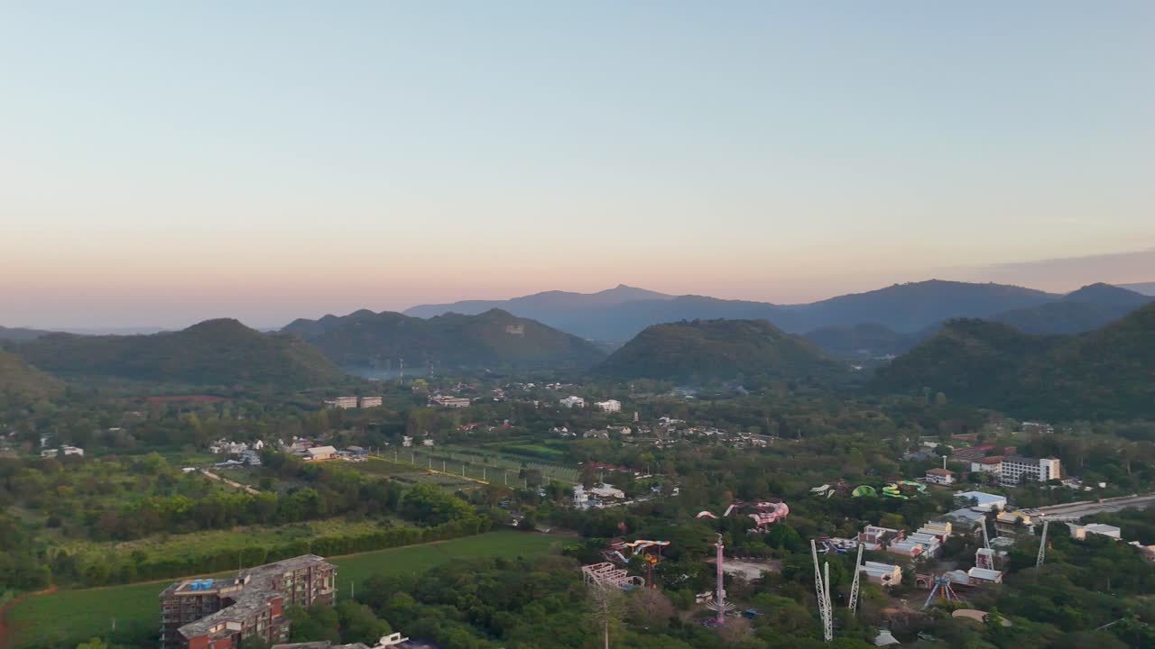 Tomada ampla de drone em panorâmica sobre um vale montanhoso exuberante e uma vila turística durante a hora dourada