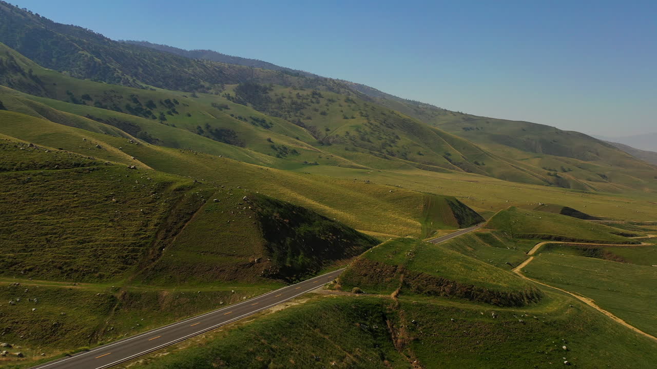 un coche solitario conduce por una carretera en las verdes estribaciones de las montañas tehachapi en el sur de california - vista aérea