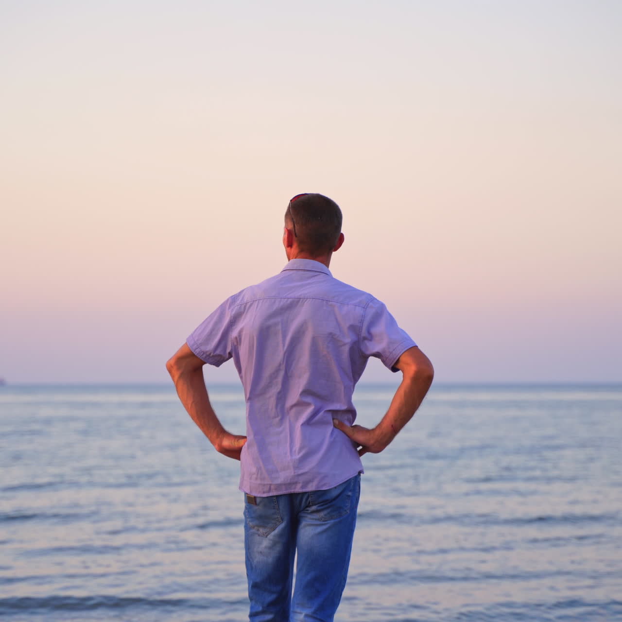 Man standing back on the beach and looking at sea in the evening. Young man in t-shirt and jeans resting near the sea. Handsome man enjoys the nature and breathes fresh air.
