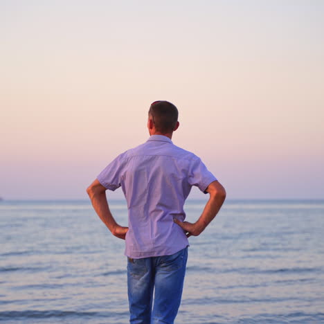 man standing back on the beach and looking at sea in the evening. young man in t-shirt and jeans resting near the sea. handsome man enjoys the nature and breathes fresh air.