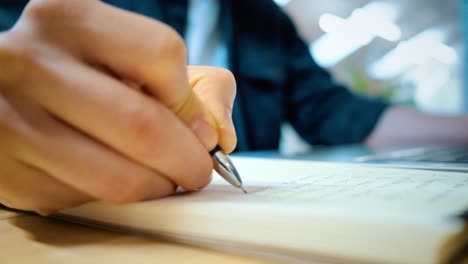 male hand writes in a notebook. office background. close-up.