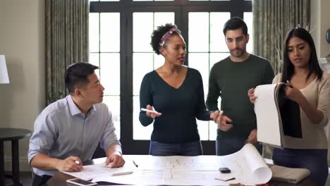 a group of four individuals engage in a collaborative brainstorming session around a table filled with plans and documents. they discuss ideas and share insights in a homey environment.