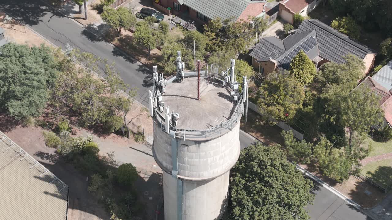 Drohnenaufnahme eines Wasserturms mit 5G-Antennen inmitten einer Vorstadtlandschaft in Melbourne. Klarer Himmel verstärkt den weiten, ruhigen Blick von oben.