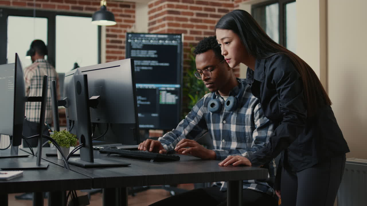 Two programers holding laptop with coding interface walking towards desk and sitting down