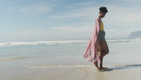 Glückliche-Afroamerikanische-Frau,-Die-Mit-Hut-Am-Sonnigen-Strand-Spaziert