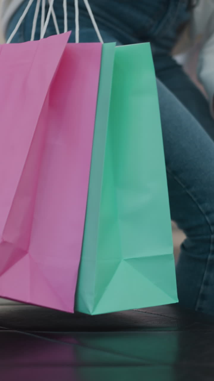 mujer se sienta con bolsas de compras en el centro comercial, luego se levanta y lleva las bolsas a mano, alejándose del asiento de cuero mientras el ambiente vibrante del centro comercial es visible en el fondo