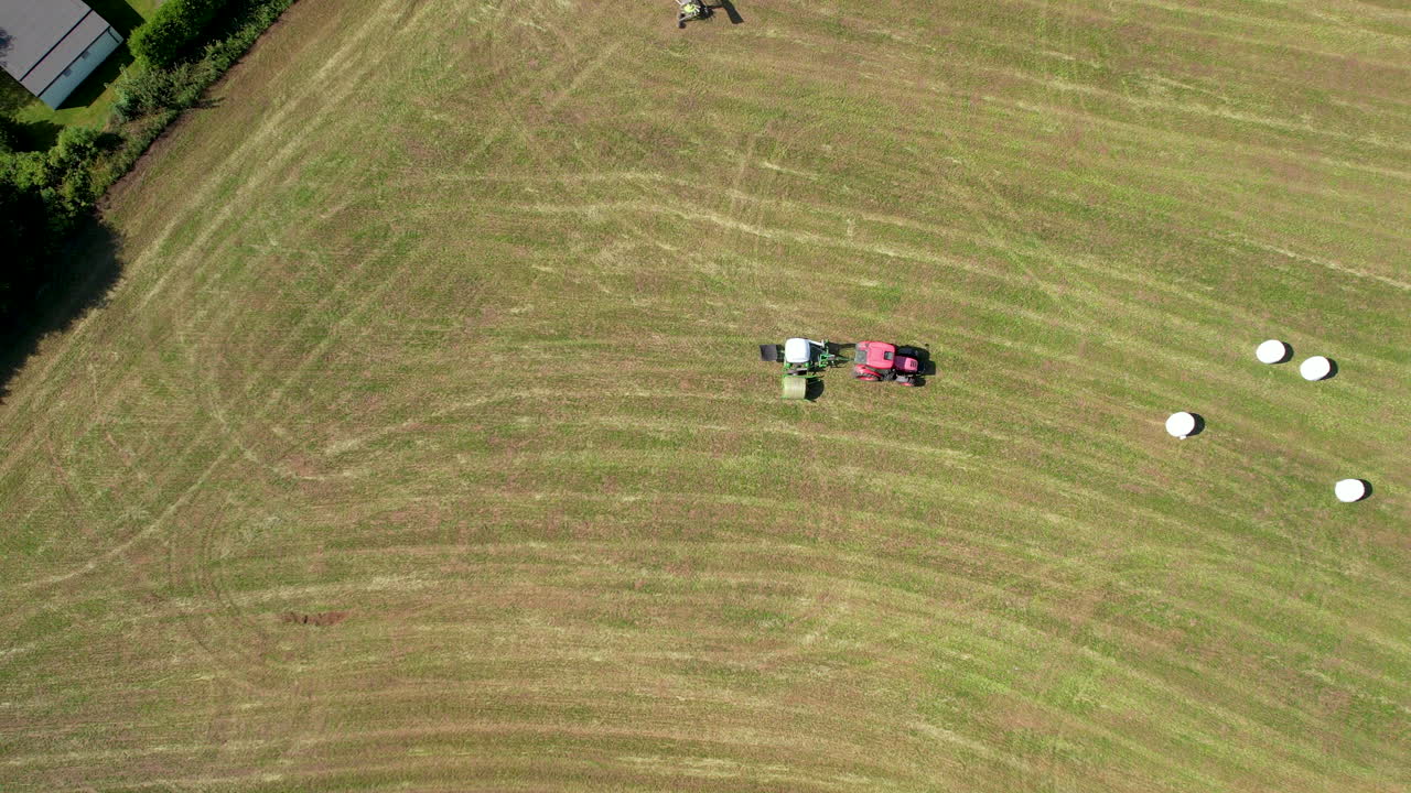 Aerial drone bird's eye view over tractors ploughing through large farmland on a sunny day