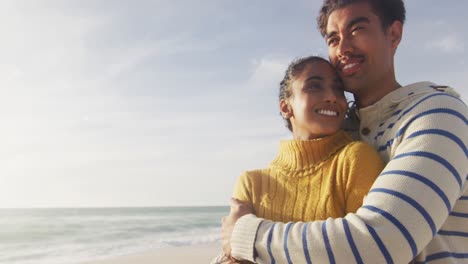 Porträt-Eines-Glücklichen-Hispanischen-Paares,-Das-Am-Strand-Steht-Und-Sich-Umarmt