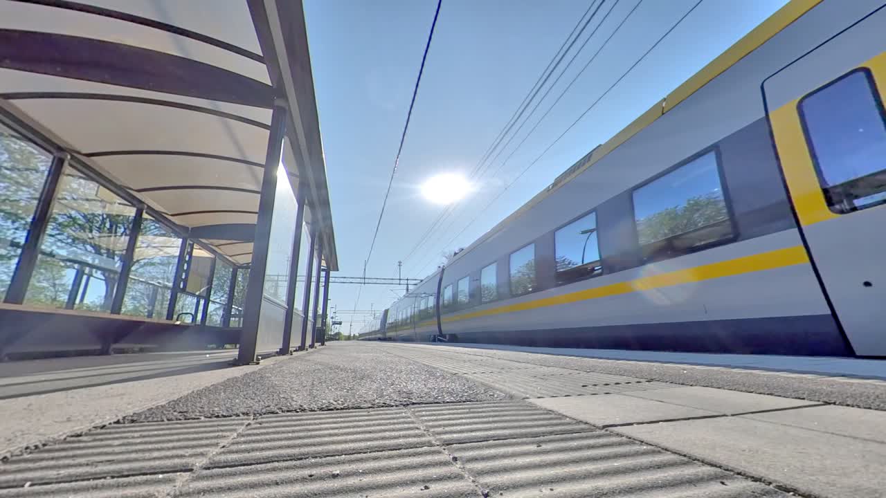 Train with yellow stipes leaves platform on sunny day, low angle, Gothenburg, Sweden