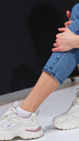 unrecognized female model in a stylish casual look. girl wears blue jeans, pink sweatshirt and white sneakers. studio shot. vertical video