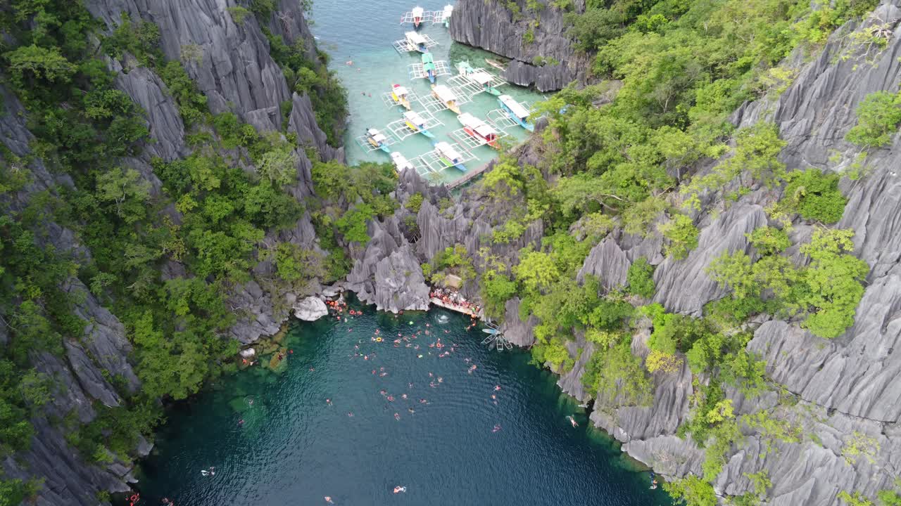 Tour boats and tourists swimming at Barracuda lake amid Karst scenery, aerial