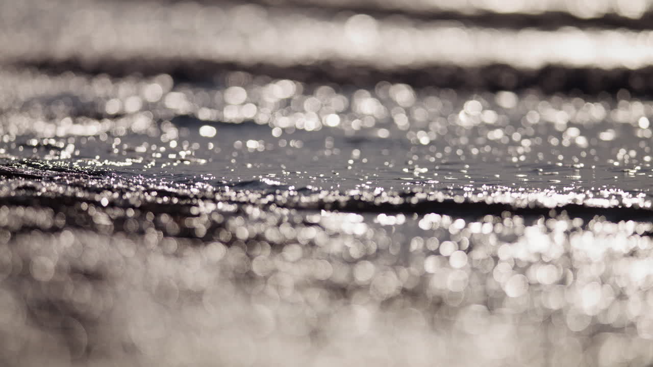 Onde scintillanti sulla costa in acque basse risplendono in una luminosa luce argentata diurna, acqua sullo sfondo, slow motion, profondità di campo ridotta