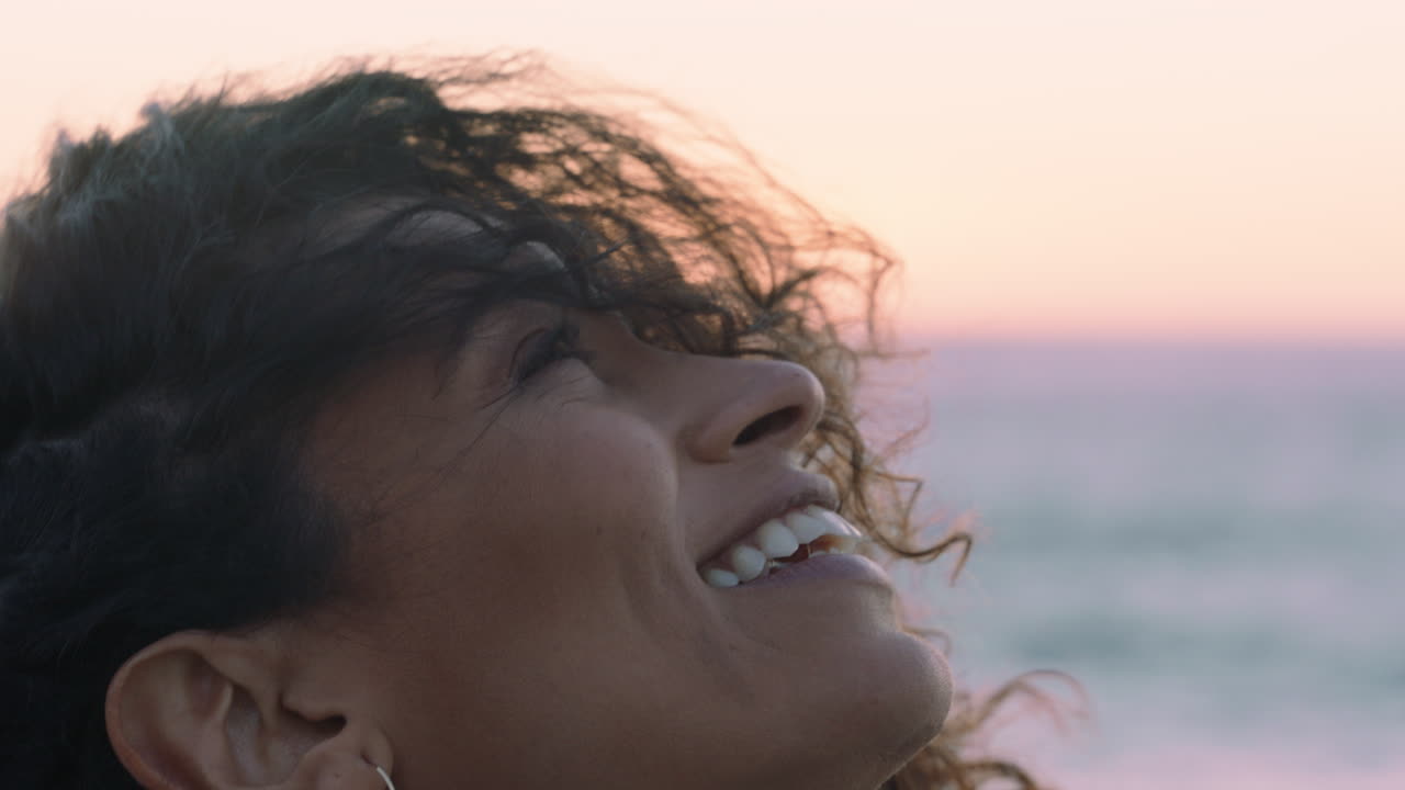 retrato de cerca de una hermosa mujer hispana mirando hacia arriba explorando la atención contemplando la espiritualidad con el viento soplando el cabello disfrutando de la pacífica playa al atardecer