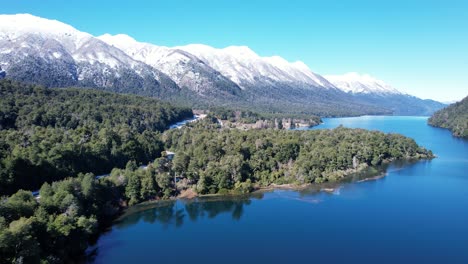 Massive-mountain-range-with-white-tops-and-green-forest-bellow,-aerial-view