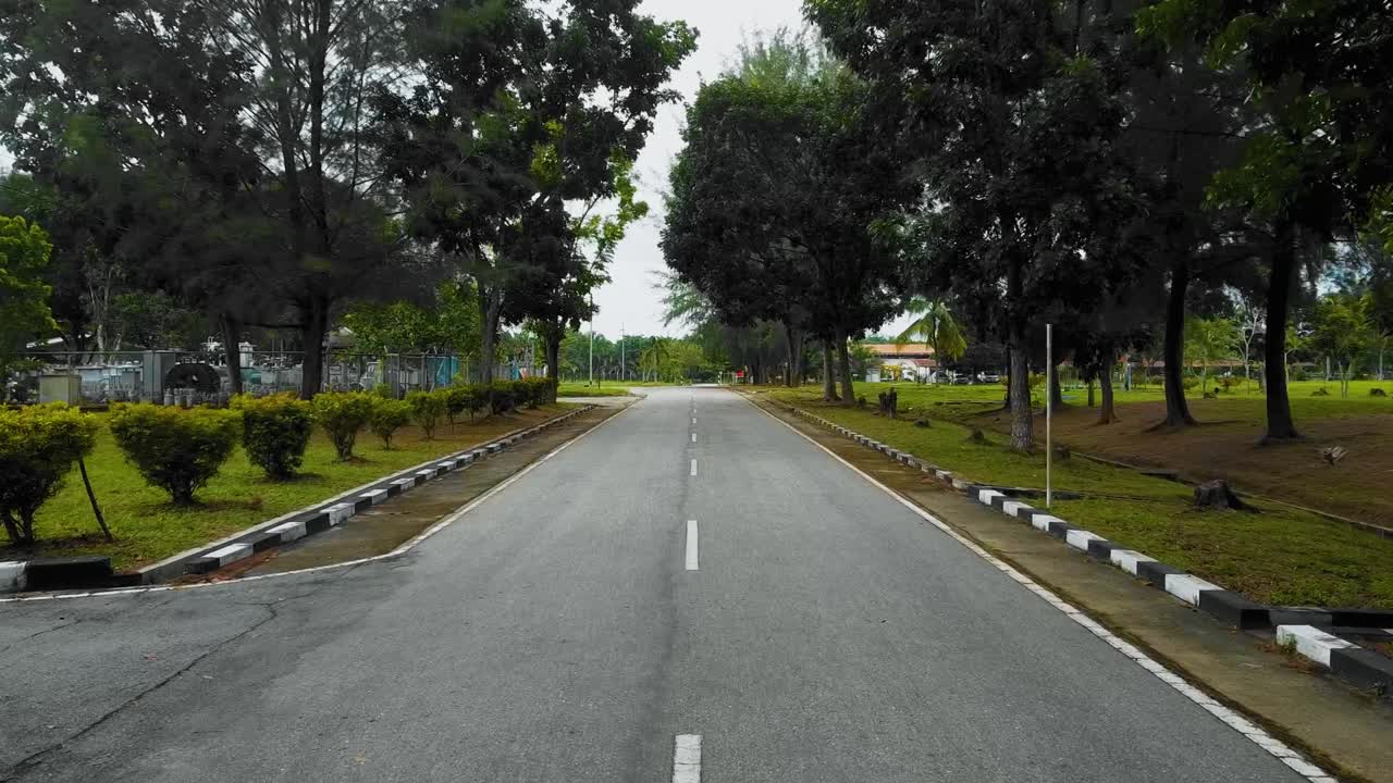 Seorang pria berolahraga dan berlari di tengah jalan, direkam dari atas menggunakan drone DJI, dengan banyak pohon tinggi dan rumput hijau di sekitarnya, menggunakan sepatu lari Nike.
