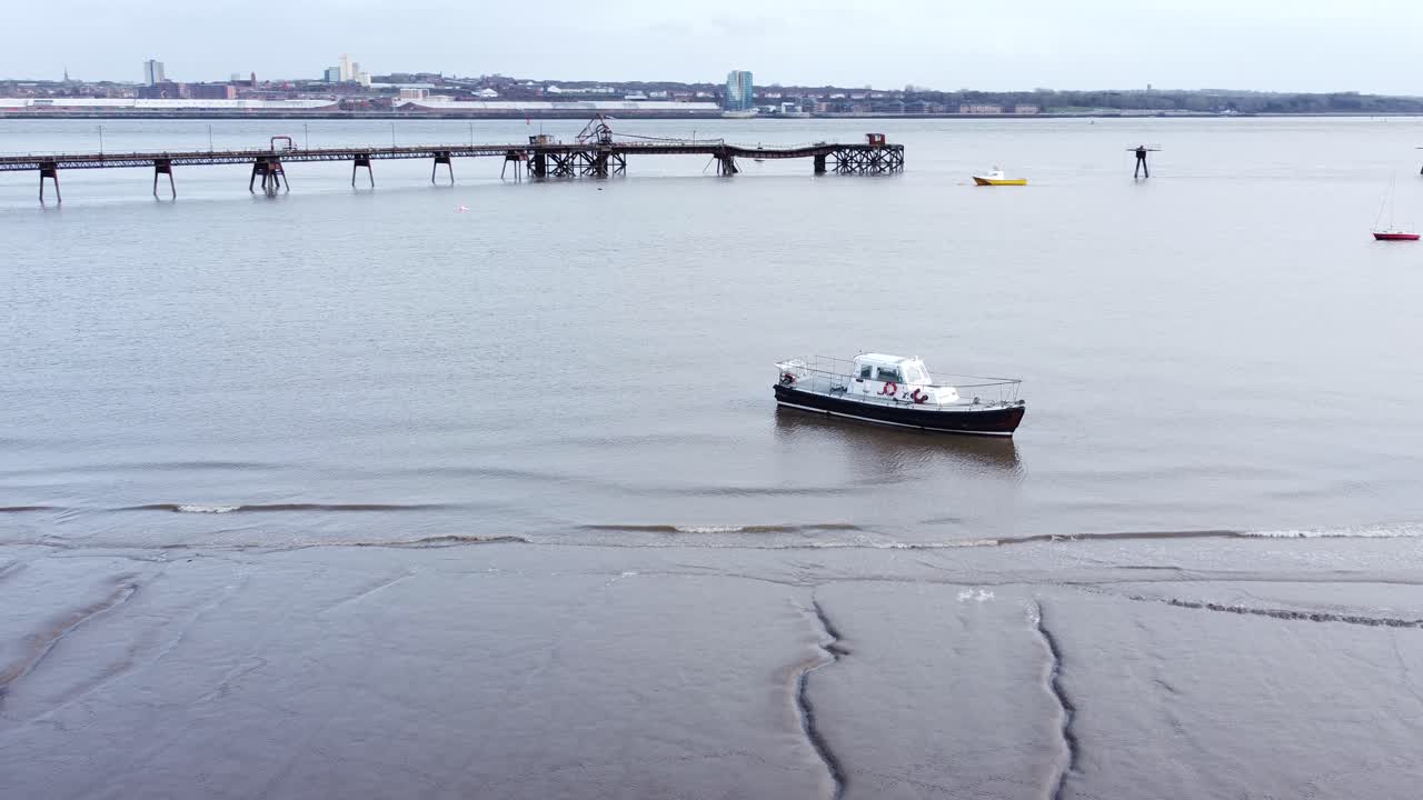 Luftfoto af fritidssejlbåd fortøjet ved Liverpools sandede byhavns kystlinje, lav omdrejning til højre