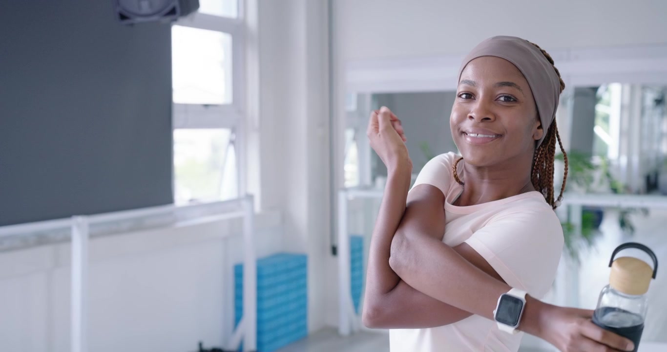 Thirsty, African American woman drinking from bottle, doing warmup swings at gym, copy space