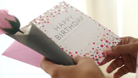 person holding a happy birthday card and a single rose
