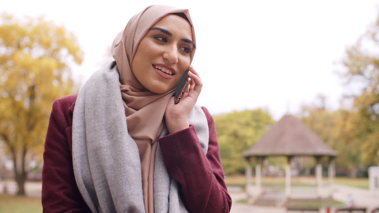 British Muslim Woman Using Mobile Phone In Park
